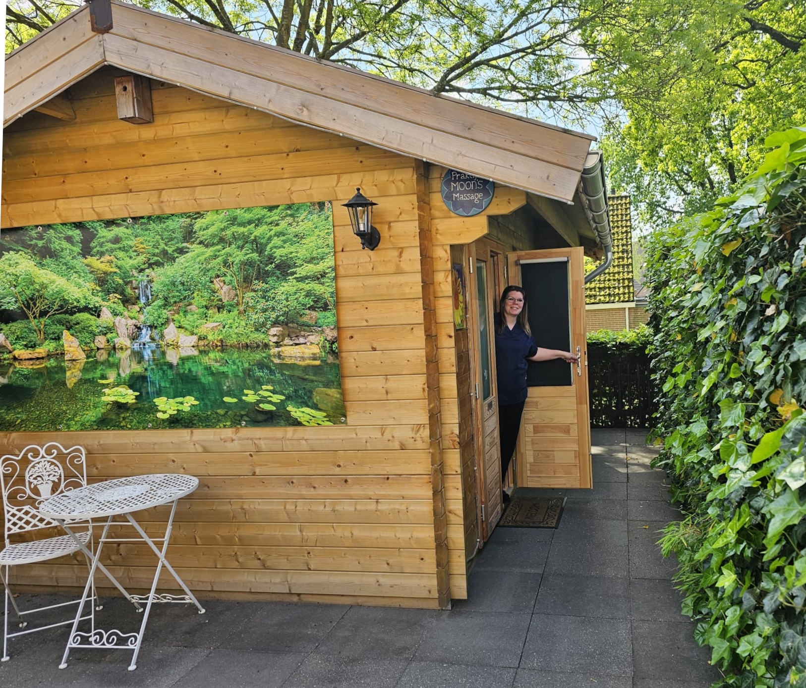 Buitenkant van de houten praktijkcabine Moon's Massage in Apeldoorn, met naam op het bord boven de deur en uitnodigende deuropening